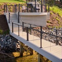 A contemporary dock structure featuring tiered seating and railings, situated by a serene lakeside. The setting includes lush greenery and a rocky shoreline, with clear skies overhead. The design emphasizes clean lines and functionality, ideal for relaxation or outdoor gatherings.